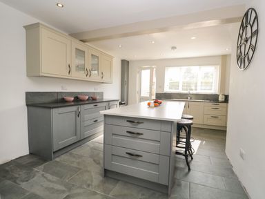 A kitchen with gray lower cabinets cream upper cabinets a central island and large wall clock at 26 Hycemoor Way Bootle Near Millom