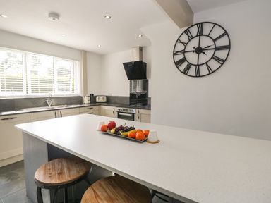 A kitchen with an island countertop and stools and a large clock on the wall at 26 Hycemoor Way Bootle Near Millom