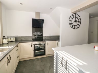 A kitchen with white cabinets a gray countertop an oven stove kettle toaster and a black wall clock at 26 Hycemoor Way Bootle Near Millom