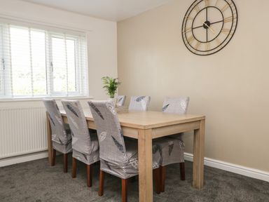 A dining area with a wooden table six chairs a large wall clock and a window with blinds at 26 Hycemoor Way Bootle Near Millom