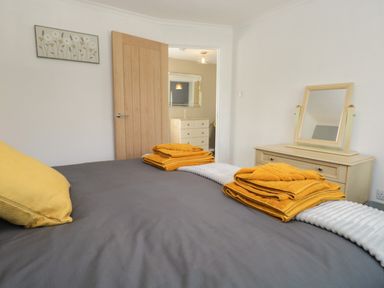 A bedroom with a bed, yellow towels, a wooden dresser with a mirror, and a wall painting at 26 Hycemoor Way Bootle Near Millom