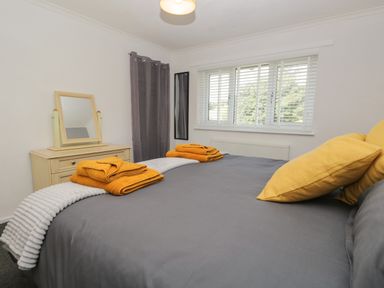 A bedroom with a bed with yellow pillows and towels a dresser with a mirror and a window with blinds at 26 Hycemoor Way Bootle Near Millom
