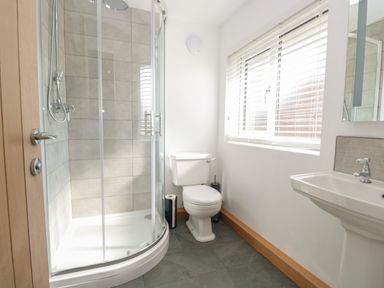 A bathroom with a glass shower enclosure, a toilet, a sink, and a window with blinds at 26 Hycemoor Way Bootle Near Millom