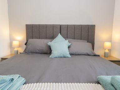 A bed with gray bedding two teal pillows and bedside tables with lamps at 26 Hycemoor Way Bootle Near Millom