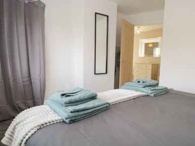 A bedroom with a bed with folded towels on a gray bedspread a tall mirror on the wall and an open door showing a dresser and mirror at 26 Hycemoor Way Bootle Near Millom