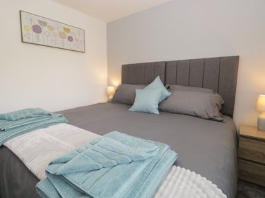A bedroom with a double bed with grey bedding and blue towels on the bed at 26 Hycemoor Way Bootle Near Millom