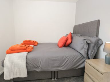 A bedroom with a grey bed a wooden nightstand with a lamp and folded orange towels at 26 Hycemoor Way Bootle Near Millom