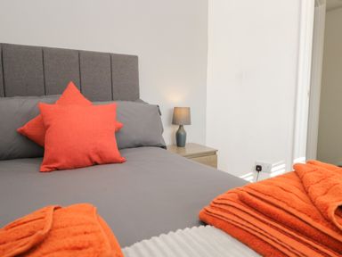 A bedroom with a bed featuring gray bedding and orange pillows with a bedside table and lamp at 26 Hycemoor Way Bootle Near Millom