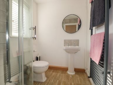 A bathroom with a toilet sink round mirror shower and towel rack with pink and gray towels at 26 Hycemoor Way Bootle Near Millom
