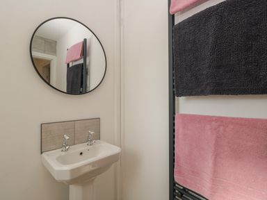 A bathroom with a white sink and round mirror with pink and black towels hanging at 26 Hycemoor Way Bootle Near Millom