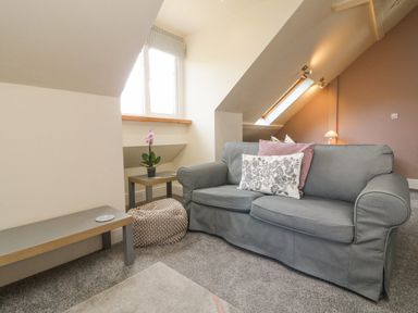 A sitting area with a gray sofa with cushions a small side table with a flower and a bench in an attic room at Nattaden @ Fourwinds Meldon near Okehampton
