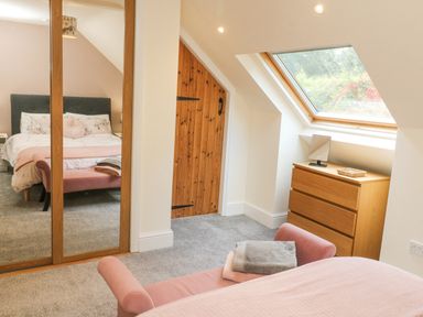 A bedroom with a bed reflected in a mirrored wardrobe a wooden door a chest of drawers and a skylight window at Nattaden @ Fourwinds in Meldon near Okehampton