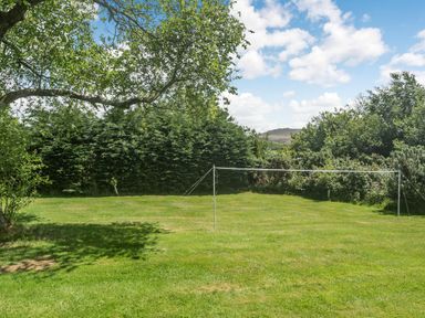 A grassy backyard with a badminton net surrounded by trees and bushes at Nattaden Fourwinds in Meldon near Okehampton