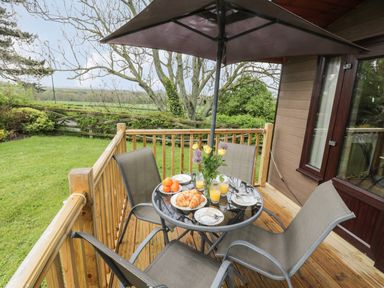 A wooden deck with a round glass table set for breakfast under a large umbrella at Holly Lodge in Liverton