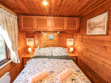 A bedroom with a bed with animal print bedding and pink towels on it surrounded by wooden walls and ceiling at Holly Lodge in Liverton