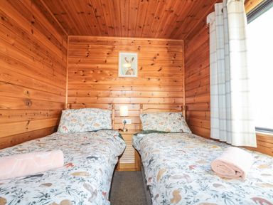 A bedroom with two single beds with patterned bedding and a wooden wall at Holly Lodge in Liverton