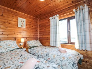 A wooden bedroom with two single beds with animal print bedding a lamp a window with curtains and a rabbit picture on the wall at Holly Lodge in Liverton