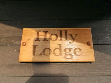 A wooden sign with the text Holly Lodge mounted on a dark wooden surface at Holly Lodge in Liverton
