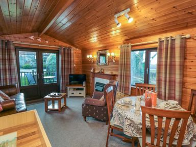 A wooden living room with a dining table set curtains a sofa chairs and a television at Holly Lodge in Liverton