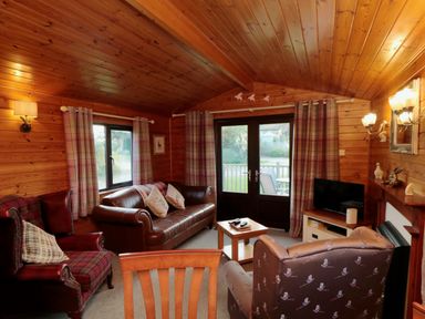 A living room with wood-paneled walls and ceiling with sofas and armchairs around a coffee table at Holly Lodge in Liverton
