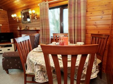 A dining area with a wooden table and chairs set with dishes and a jug in a wooden cabin with plaid curtains at Holly Lodge in Liverton