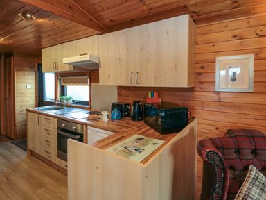 A wooden kitchen with cabinets a sink microwave kettle toaster and oven at Holly Lodge in Liverton