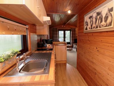A kitchen with a sink toaster and microwave leading to a living area with coffee table and curtains at Holly Lodge in Liverton