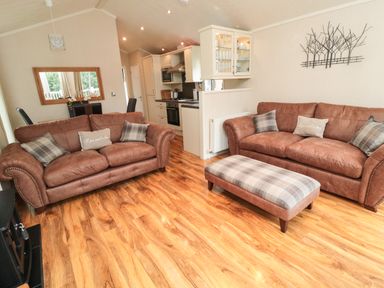 A living room with two brown sofas a plaid ottoman a dining table and kitchen area at Number 43 Burnside Lodge in Felton