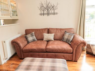 A brown sofa with three cushions and a plaid ottoman in a living room at Number 43 Burnside Lodge in Felton