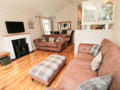 A living room with brown sofas a plaid ottoman wooden floor and a wall mounted tv at Number 43 Burnside Lodge in Felton