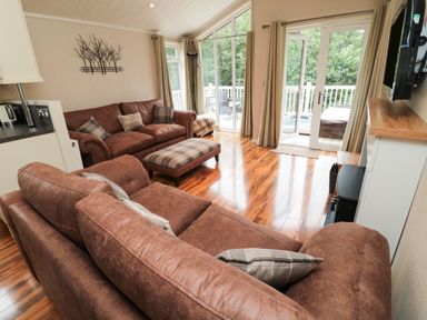 A living room with brown sofas a plaid ottoman wooden floor and glass doors leading to a balcony at Number 43 Burnside Lodge in Felton