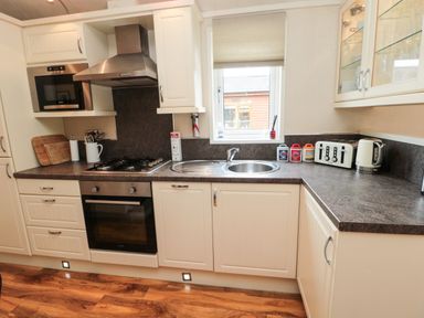 A kitchen with white cabinets a gas stove an oven microwave sink toaster kettle and containers on the counter at Number 43 Burnside Lodge in Felton