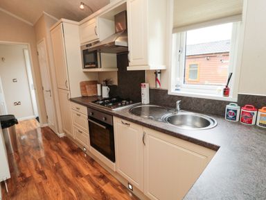 A kitchen with brown countertop white cabinets a stove oven microwave sink and window at Number 43 Burnside Lodge in Felton