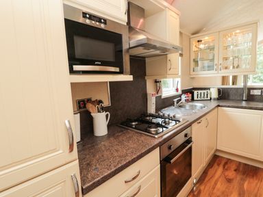 A kitchen with cream cabinets, granite countertops, a gas stove, oven, microwave, sink, toaster, kettle and glass cabinet at Number 43 Burnside Lodge in Felton