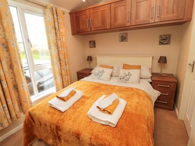 A bedroom with a bed covered with orange blanket and pillows with rabbit prints two bedside tables with lamps and wooden cabinets above the bed at Number 43 Burnside Lodge in Felton
