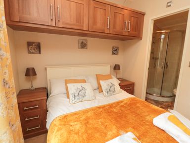 A bedroom with a double bed with orange and white bedding two bedside tables with lamps and a bathroom with a shower at Number 43 Burnside Lodge in Felton