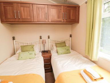 A small bedroom with two single beds with green pillows and yellow blankets at Number 43 Burnside Lodge in Felton