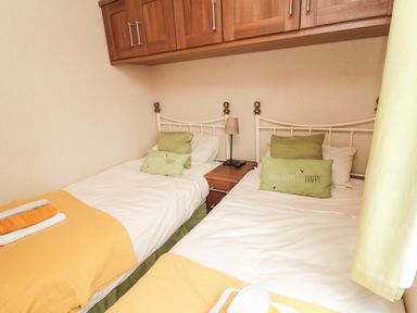 A small bedroom with two single beds separated by a wooden nightstand with a lamp and remote at Number 43 Burnside Lodge in Felton