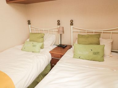 A bedroom with two single beds with green cushions and a wooden nightstand with a lamp and remote at Number 43 Burnside Lodge in Felton