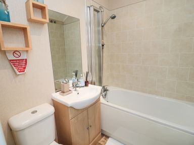 A bathroom with a toilet sink with wood cabinet mirror bathtub and shower at Number 43 Burnside Lodge in Felton