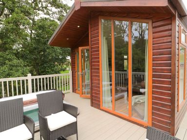 An outdoor deck with black wicker chairs cushions a hot tub and large windows of a wooden cabin at Number 43 Burnside Lodge in Felton
