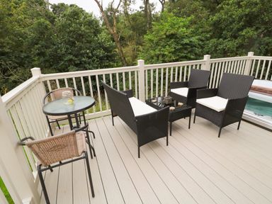 An outdoor deck with a glass table and chairs plus black wicker seating at Number 43 Burnside Lodge in Felton