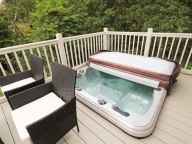 An outdoor deck with a hot tub and two cushioned wicker chairs at Number 43 Burnside Lodge in Felton