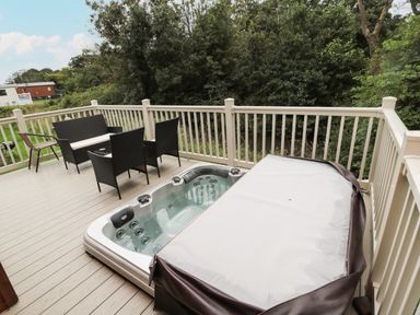 An outdoor deck with a hot tub and patio furniture surrounded by trees at Number 43 Burnside Lodge in Felton