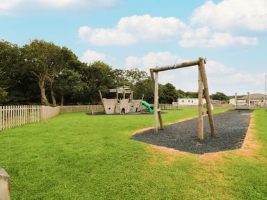 An outdoor playground with a wooden play structure shaped like a ship and a swing frame on grass at Number 43 Burnside Lodge in Felton