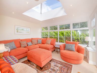 A living room with orange sofas a skylight and large windows showing greenery at West Bay Holiday Home in West Bay