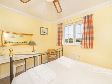 A bedroom with a metal bed frame two folded towels on the bed a white desk with a lamp and mirror and a window with checkered curtains at West Bay Holiday Home in West Bay