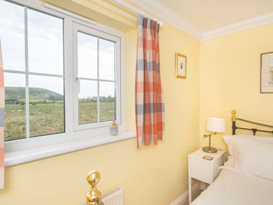 A bedroom corner with a window showing a countryside view and a bed with a bedside table and lamp at West Bay Holiday Home in West Bay