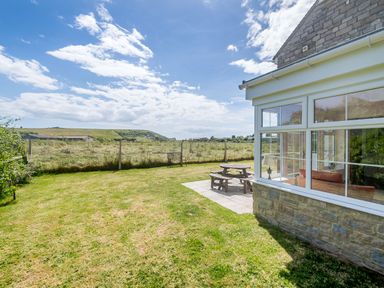 A garden with grass and a wooden picnic table beside a house with large windows at West Bay Holiday Home in West Bay