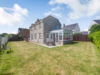 A stone house with a glazed conservatory and a lawn with outdoor furniture at West Bay Holiday Home in West Bay